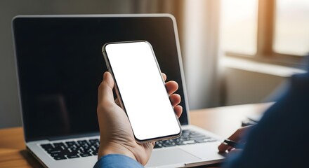 Person holding smartphone with blank screen in front of laptop