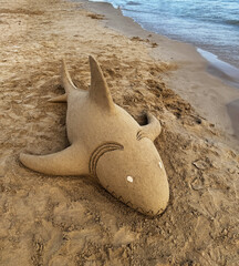 A dolphin made of sand on the beach. A sand dolphin on the seashore.