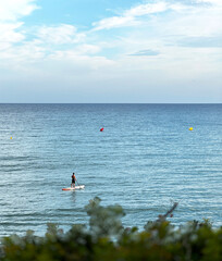 A calm blue sea with two surfers walking into the distance