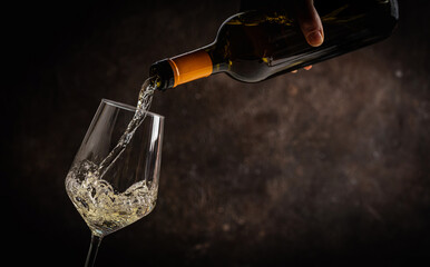 Fototapeta premium Pouring white wine into the glass on rustic dark background. Pour alcohol, winery concept.