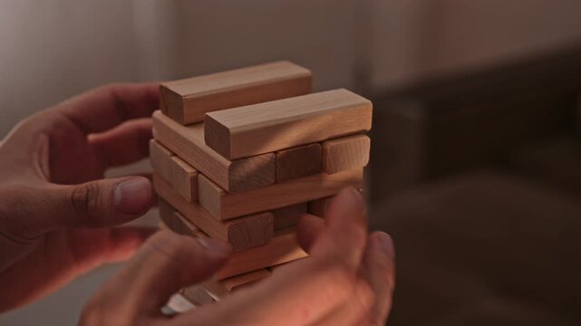 Close-up of hands playing a wooden block stacking jenga game indoors, showing the moment a tower collapses into hands after a piece is removed