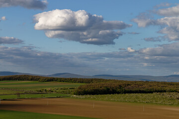 Naklejka premium Picturesque landscape with fields, trees, and a bright blue sky dotted with clouds.