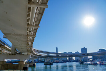 逆光の中に輝く太陽と大きく湾曲する高速道路の高架橋