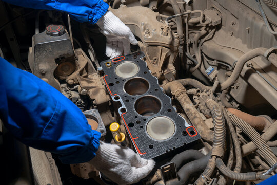 Close-up of a mechanic&rsquo;s gloved hands installing a new cylinder head gasket on an open engine block during vehicle repair.