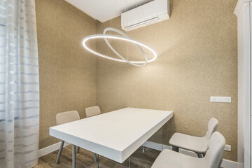 A dining area shows an empty white table with four chairs in a plain room. A round light hangs above the table, and the walls are beige