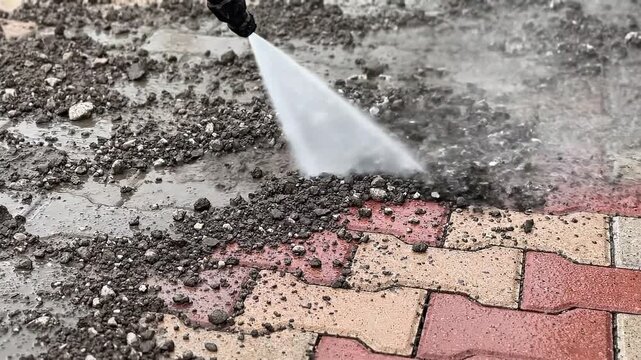 Worker using a professional high pressure washer to clean dirt and moss from stone block paving on a residential driveway area