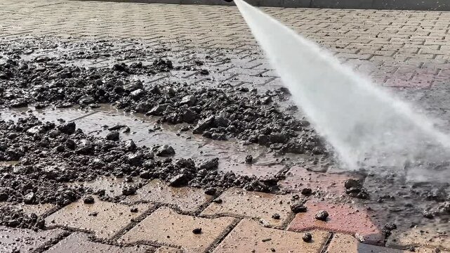 Close up of a power washer wand spraying water to remove grime from a paved walkway during a professional outdoor cleaning service