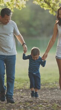 Cute young family walking in the park - parents holding their little son by his hands