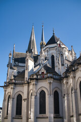 Fototapeta premium Gothic Cathedral Spires and Apse Detail - Ornate Gothic cathedral exterior detail showing multiple stone spires, pinnacles, and intricate tracery against a stark, clear blue sky.