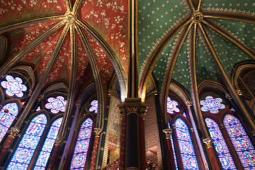 Obraz premium Gothic Vaults and Murals of Sainte-Chapelle - Low-angle view of richly painted Gothic rib vaulting in red, gold, and teal, alongside a large crucifixion mural and stained glass windows.