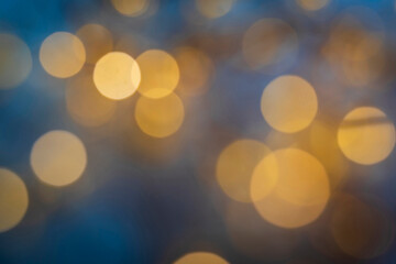 Obraz premium Abstract golden bokeh circles on blue background, soft blur. Warm yellow bokeh light circles glowing against a dark blue background in a soft focus.