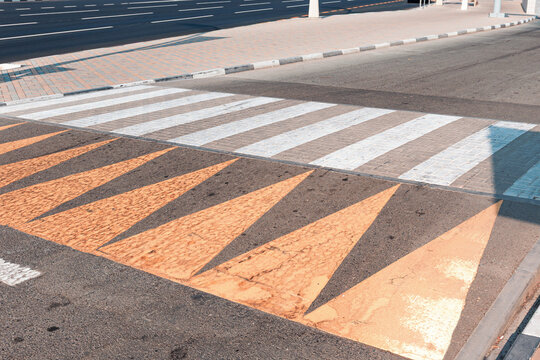 Yellow shark teeth road markings indicating a speed bump leading to a white striped zebra crosswalk on an urban street
