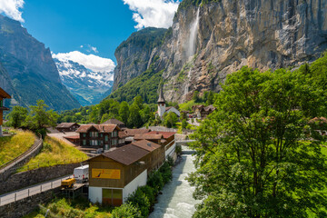 Wide panoramic view of Lauterbrunnen Valley with lush meadows, traditional village houses, and a powerful waterfall in the Swiss Alps