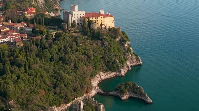 Aerial view of Castello di Duino on cliffs near Trieste. Dramatic Adriatic Sea coast, Sentiero Rilke path, and medieval architecture. Cinematic 4K drone footage of Italian heritage and coastal beauty.