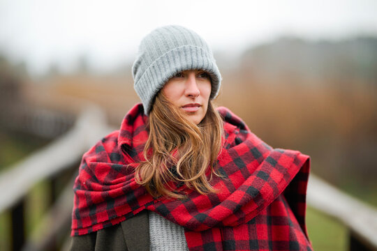 Blonde woman wrapped in plaid blanket scarf on rainy day