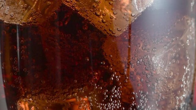 Extreme macro shot of a tall, chilled glass filled with Coca-Cola, focusing on the mesmerizing stream of tiny carbonation bubbles rising rapidly through the dark amber liquid. Ice cubes float, partial