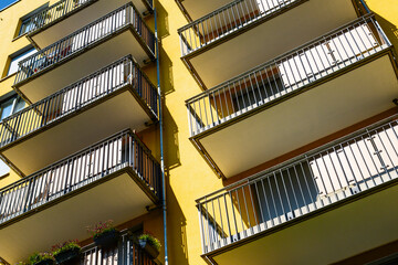 Modern yellow apartment building facade with balconies and geometric shadows