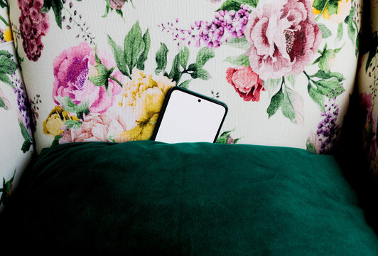 Smartphone hidden behind green cushion on floral couch