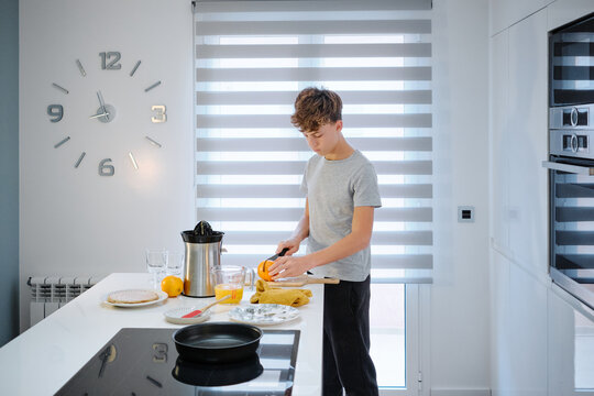 Boy preparing fresh orange juice in modern kitchen
