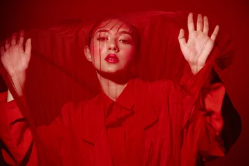 Fotobehang Onderzeeër Fashionable young woman in red outfit behind red mesh fabric. Creative beauty concept with strong color contrast on a red background. Artistic high fashion studio shot.  © SHOTPRIME STUDIO