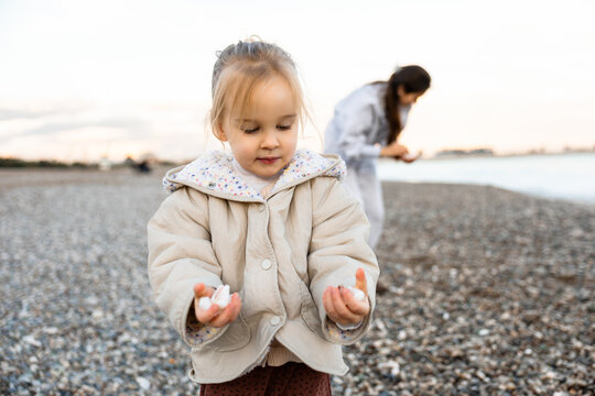 Little girl exploring shells on a pebble beach