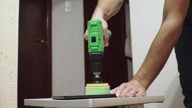 Hands of caucasian man with power drill, polishing tablet with paste using foam attachment, close up. Home restoration of device and scratch removal.