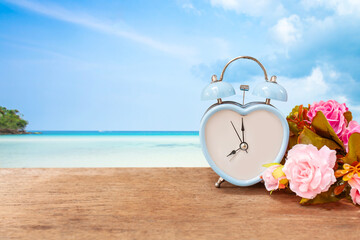 Retro clock with flowers on wooden table over blurred blue sea.