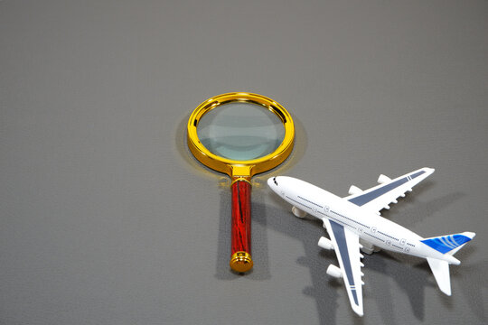 Magnifying glass examining a small white airplane model symbolizing travel investigation, inspection, and detailed flight research concepts