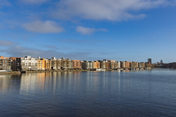 Fototapeta premium Modern residential apartment buildings at Java-eiland waterfront in Amsterdam with reflections in the IJ river under a blue sky with soft clouds
