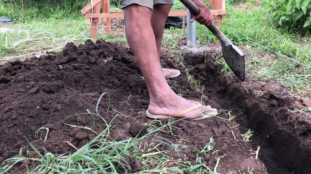 construction worker is using a metal digging bar to excavate a trench for a concrete footing.