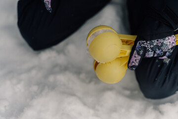 Child playing with yellow snowball maker in snow