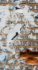 Fototapeta premium Peeling weathered posters on brick wall with exposed red bricks in urban street setting