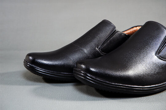 Close-up shot showcasing a pair of classic black faux leather slip-on dress shoes with textured uppers and thick rubber soles