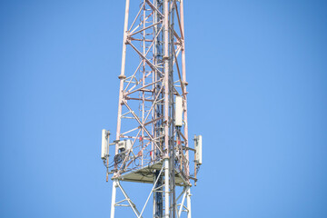 A tall tower with a white top and a blue sky in the background. The tower is a cell phone tower