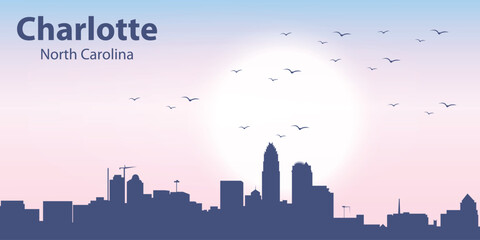 Obraz premium Stylized skyline of Charlotte, North Carolina at sunrise. Modern flat illustration with urban silhouette, pastel gradient sky, sun and flying birds. 