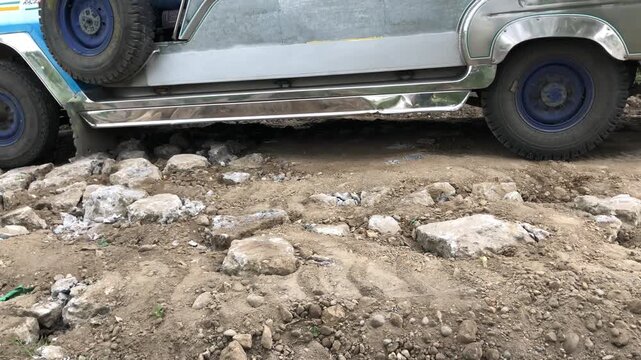 Vehicles have difficulty traveling on a rough, bumpy country road.