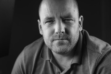 Obraz premium Close-up black and white photograph of a Middle-aged white male squinting at the camera wearing a casual collared shirt, with plain black background.