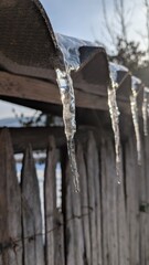 Fototapeta premium Clear hanging ice structures produce gentle shadows on fencing