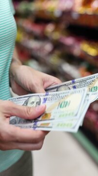 Close up view of woman hands counting cash money (American dollar USD banknotes) for shopping in supermarket. Calculating budget to spend in grocery store. Concept of financial planning in USA.