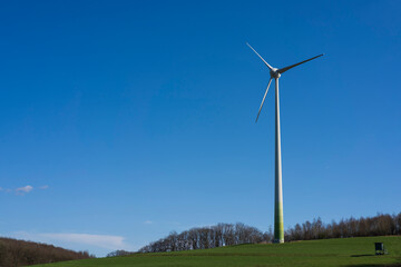 A lone wind turbine on a green hillside under a clear blue sky, minimal rural landscape concept showing real life renewable energy in Europe, Germany