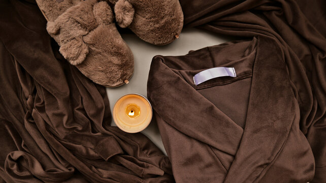 Cozy brown velvet robe, fuzzy slippers, and lit candle for ultimate relaxation and comfort