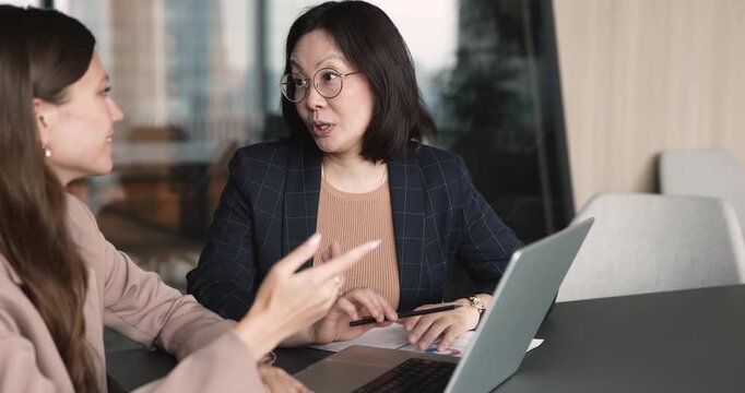 Businesswomen discussing project sit at desk with laptop during office business meeting. Consulting services, data analysis, client communication, collaborative decision making and corporate planning