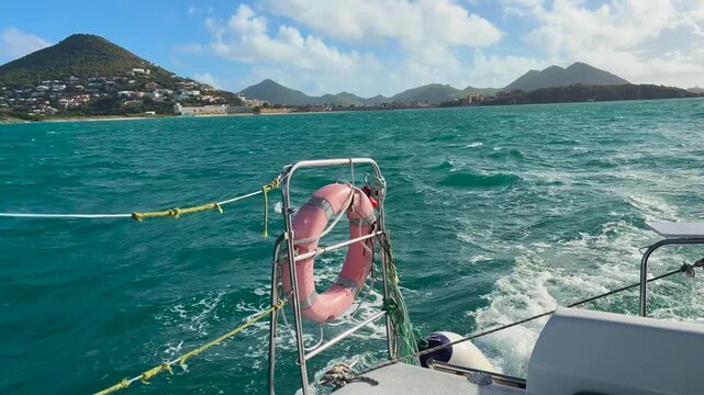 A boat trip in the Caribbean Sea near the island Saint Martin in the northeastern Caribbean. View of the island's rocky shores and ship's wake.