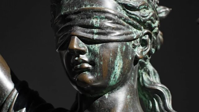 Extreme closeup of bronze statue depicting woman as justice symbol. Blindfolded female figure holds scales and sword in detailed facial pan from forehead to chin. Legal fairness concept in metallic