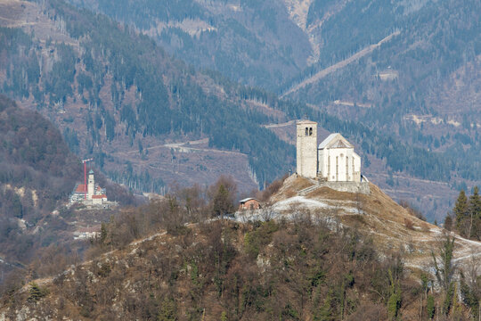 The ancient Pieve di San Floriano church on a hilltop near Illegio, Udine, Italy. Scenic panoramic view of the historical stone cathedral in the Carnic Alps mountain landscape during winter season.