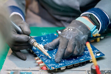 Skilled technician repairs electronic circuit board with soldering tool in workshop