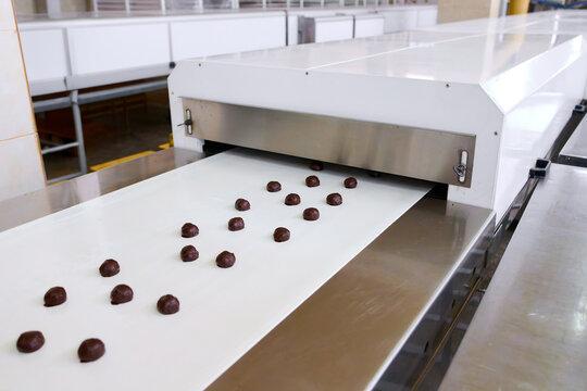 Chocolate-coated grillage nut brittle moves smoothly along the conveyor belt in a processing facility