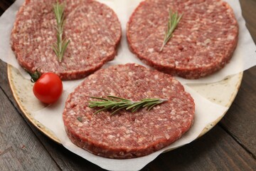 Fototapeta premium Uncooked meat patty with rosemary and tomato on wooden table, closeup