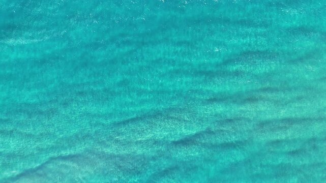 Aerial top down view of clear turquoise tropical ocean water with gentle waves and ripples, calm blue sea surface natural background drone footage