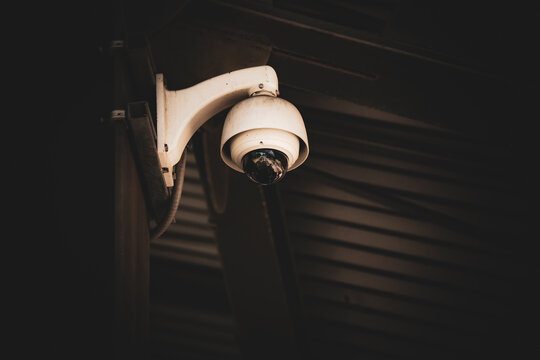 Close-up of a white dome security camera mounted outdoors under a dark roof structure